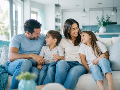 A family of four relaxing together on the sofa of an open kitchen and living space.