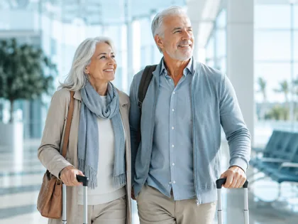 An older couple walking through an airport terminal with their luggage.